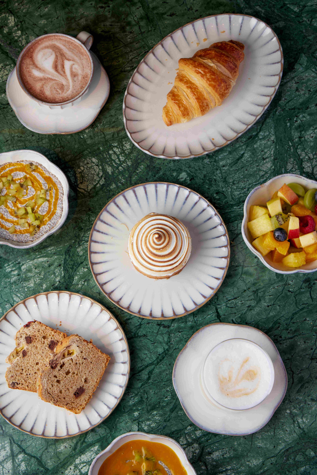 Frühstücksbuffet mit Cappuccino, Gebäck und Chia-Bowls auf grünem Marmor