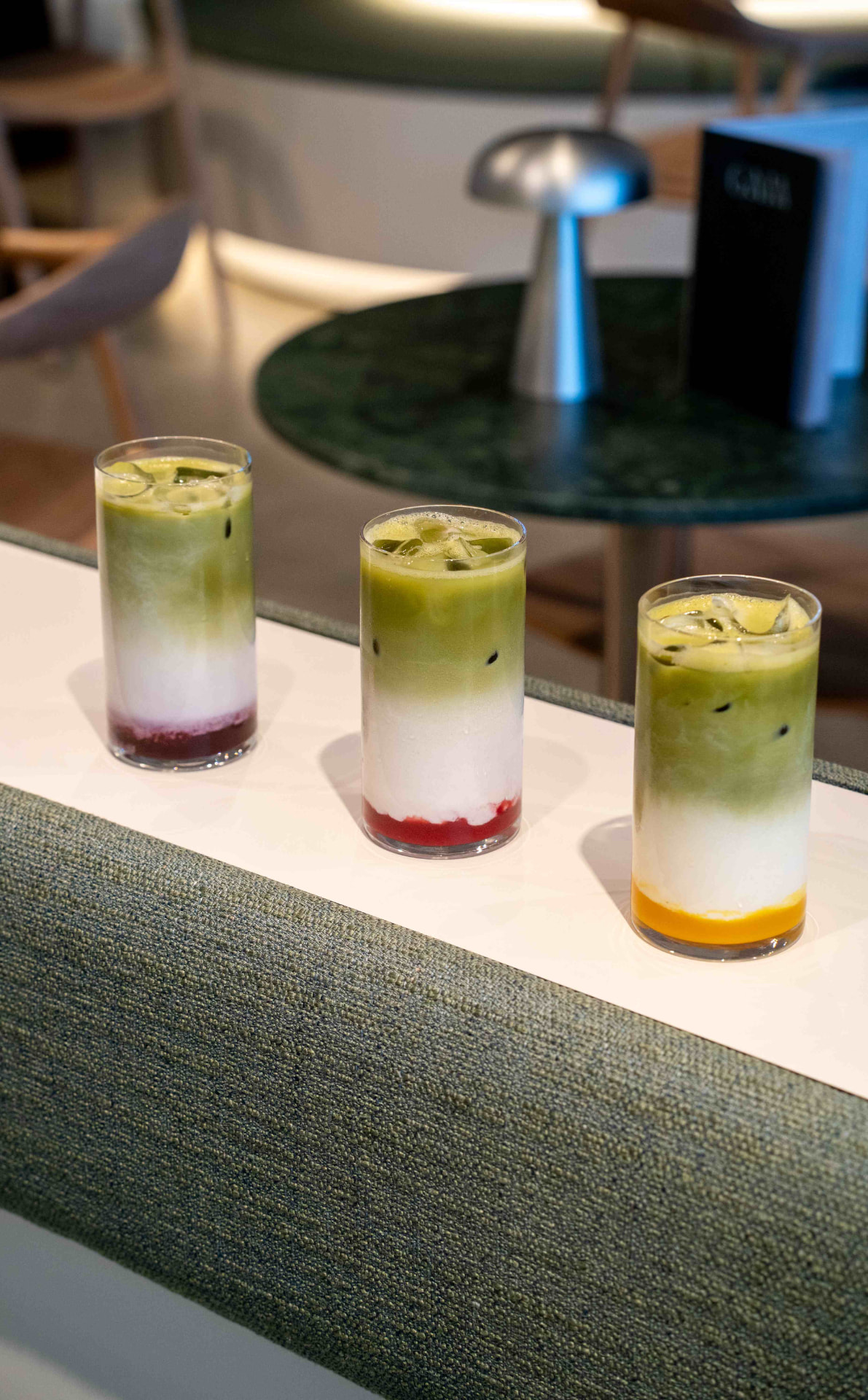 Drei geschichtete Iced-Matcha-Lattes aufgereiht auf einer Marmortheke